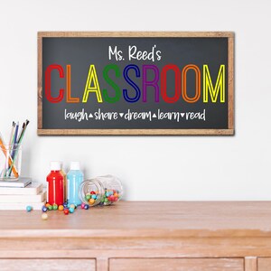 K&ouml;nnte beinhalten: Ein gerahmtes Tafelschild mit dem Text "Ms. Reed's CLASSROOM" in bunten Buchstaben. Unter dem Wort "CLASSROOM" stehen die W&ouml;rter "laugh, share, dream, learn, read". Das Schild wird auf einem Holztisch mit Kunstbedarf angezeigt.