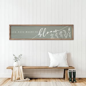 May include: A wooden sign with a sage green background and white text that reads "you were meant to bloom". The sign is decorated with white line drawings of flowers.