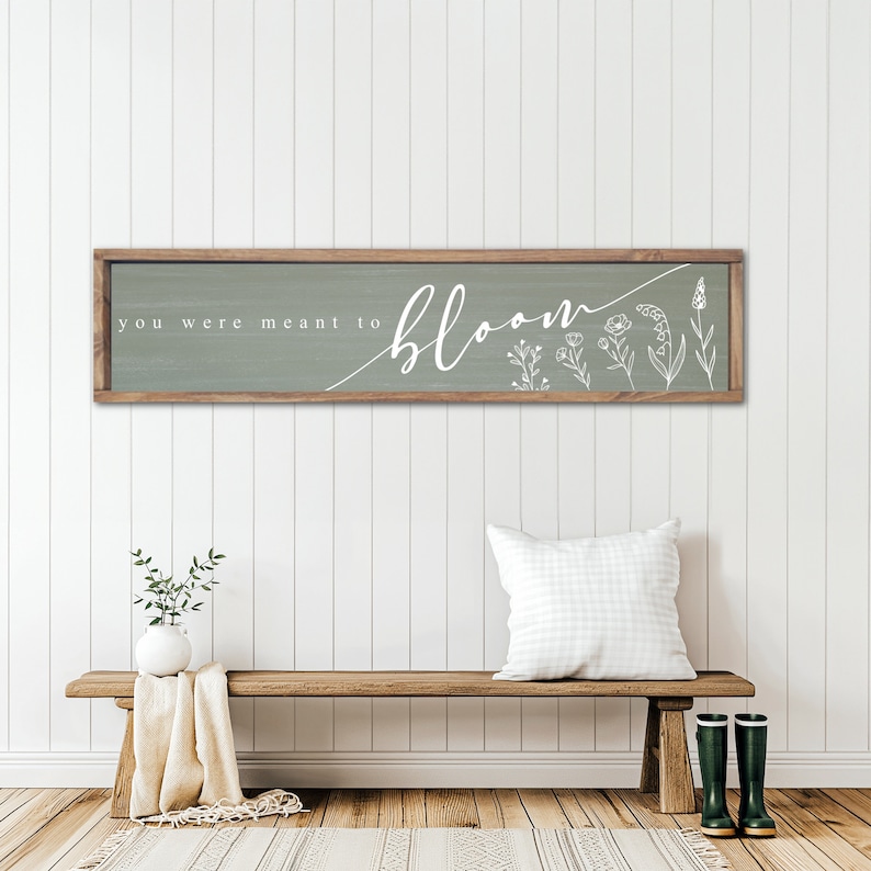 May include: A wooden sign with a sage green background and white text that reads "you were meant to bloom". The sign is decorated with white line drawings of flowers.