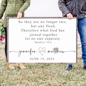 May include: A white wooden sign with a black border and a wedding quote from the Bible, Matthew 19:6. The quote reads "So they are no longer two, but one flesh. Therefore what God has joined together let no one separate." Below the quote is the couple's names, "jennifer and matthew", with a heart symbol between them. The date of the wedding, "JUNE 15, 2024", is printed below the names.