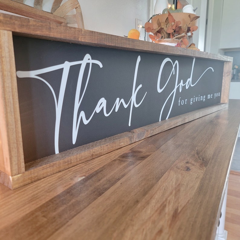 May include: A wooden framed sign with a black background and white cursive lettering that reads "Thank God for giving me you".