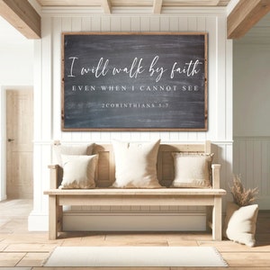 May include: A wooden sign with a black chalkboard background and white text that reads "I will walk by faith even when I cannot see 2 Corinthians 5:7". The sign is hanging on a white wall above a wooden bench with pillows.