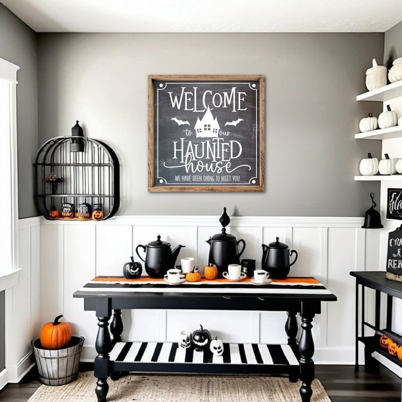 May include: A black and white striped table runner with black teapots and cups on a black table. A sign with the text "Welcome to our Haunted House. We have been dying to meet you." is on the wall behind the table.