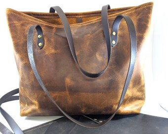 Puede incluir: Dos bolsos de mano de cuero, uno marrón y otro negro. Ambos bolsos tienen asas de cuero y herrajes de latón.