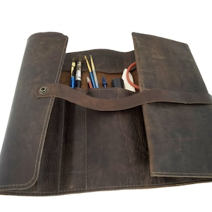 May include: A brown leather roll-up case with multiple compartments for holding art supplies, such as paintbrushes, pencils, and markers.