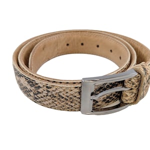 May include: A coiled belt with a snakeskin pattern in shades of tan, brown, and black. The belt has a silver-coloured rectangular buckle. The interior of the belt is a solid tan colour.