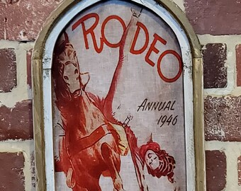 May include: A vintage-style framed poster with a red and white illustration of a rodeo event. The poster reads "Rodeo Annual 1946" and "Southwestern Exposition Fat Stock Show".