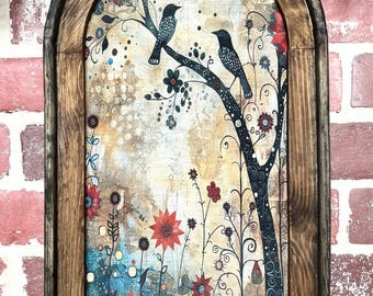 May include: A framed artwork featuring a whimsical illustration of two birds perched on a tree branch. The artwork has a rustic wooden frame and depicts a colorful garden scene with flowers in shades of red, blue, and orange.