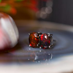 May include: A pair of black metal stud earrings with red and black opal gemstones.