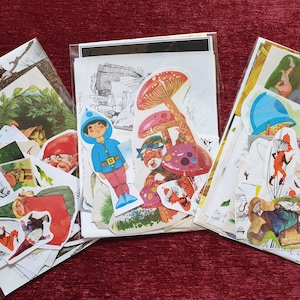 May include: Three clear plastic bags filled with vintage-style ephemera. The ephemera includes colourful illustrations of gnomes, mushrooms, and a boy in a blue hat. The background is a deep red.