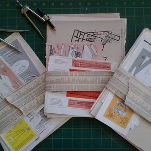 May include: A stack of papers containing architectural drawings and plans, wrapped in newspaper and tied with twine. The papers are on a green cutting mat with a compass and ruler.