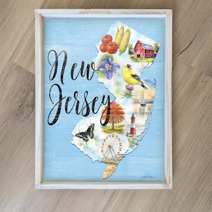 May include: A framed wooden sign featuring a map of New Jersey with illustrations of local landmarks and produce. The words "New Jersey" are written in a cursive font over a light blue background.