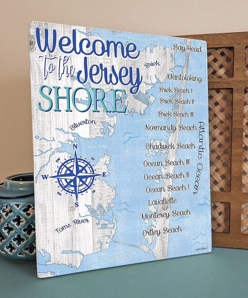 Puede incluir: Un letrero de madera azul y blanco con un mapa de la costa de Jersey. El letrero dice "Bienvenido a la costa de Jersey" e incluye los nombres de varias ciudades y playas a lo largo de la costa. Una br&uacute;jula est&aacute; en el centro del mapa.