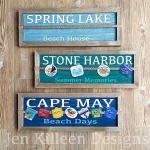 May include: Three wooden signs with rope accents and various beach-themed designs. The top sign reads "SPRING LAKE Beach House". The middle sign reads "STONE HARBOR Summer Memories" and features small round pins with beach-themed imagery. The bottom sign reads "CAPE MAY Beach Days" and features a row of small round pins with beach-themed imagery.