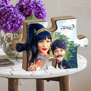 K&ouml;nnte beinhalten: Ein h&ouml;lzernes Puzzle-Teil in Herzform mit einem Foto einer Frau und eines Jungen. Das Puzzle-Teil ist braun und hat einen wei&szlig;en Hintergrund. Das Foto zeigt eine Frau mit dunklen Haaren und einen Jungen mit braunen Haaren. Die Frau tr&auml;gt ein wei&szlig;es Hemd und der Junge tr&auml;gt ein schwarzes Hemd. Der Text "I love you to the Moon and back" ist auf dem Puzzle-Teil geschrieben.