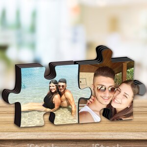 K&ouml;nnte beinhalten: Ein Holzpuzzle-Bilderrahmen mit zwei separaten Teilen, die ineinander passen. Der Rahmen zeigt ein Paar auf zwei verschiedenen Fotos. Ein Foto zeigt ein Paar im Wasser, das andere Foto zeigt ein Paar, das zusammen posiert.