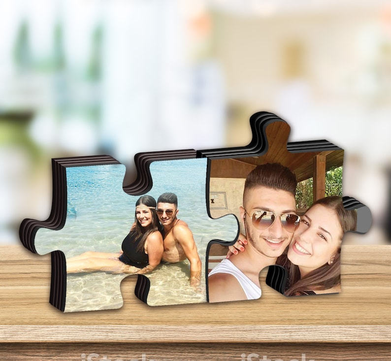 K&ouml;nnte beinhalten: Ein Holzpuzzle-Bilderrahmen mit zwei separaten Teilen, die ineinander passen. Der Rahmen zeigt ein Paar auf zwei verschiedenen Fotos. Ein Foto zeigt ein Paar im Wasser, das andere Foto zeigt ein Paar, das zusammen posiert.
