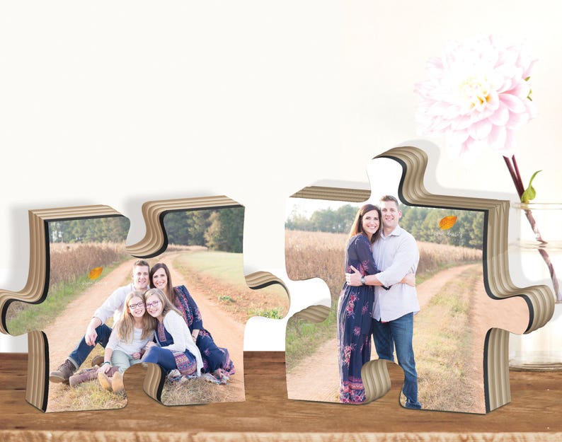 May include: Two wooden jigsaw pieces with photos of families. The left piece shows a family of four sitting on a path in a field. The right piece shows a couple standing on a path in a field.
