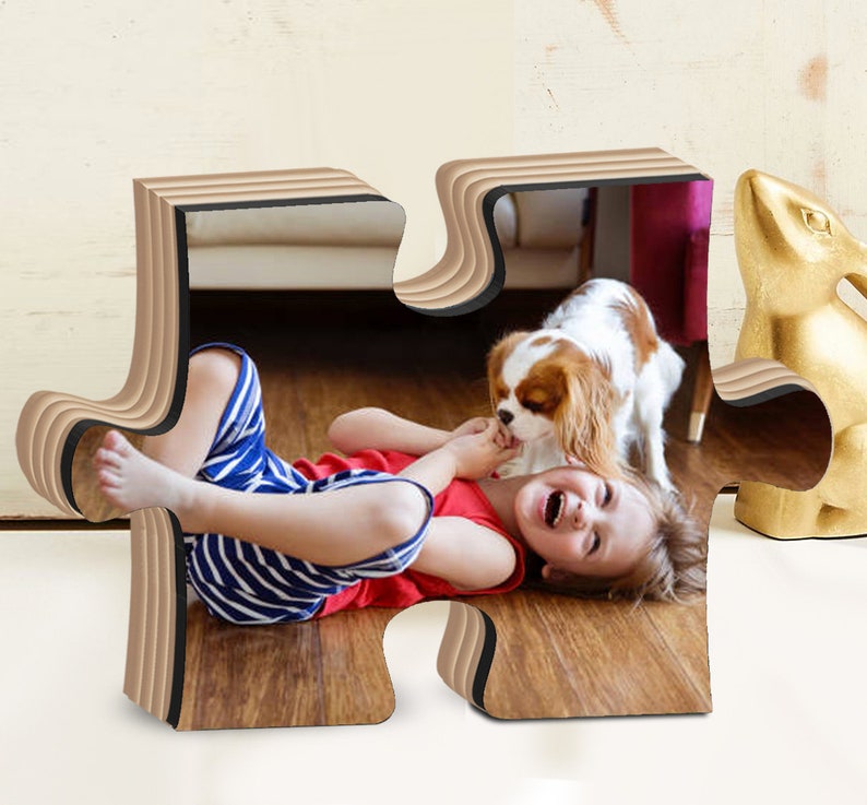 May include: A wooden puzzle piece photo frame with a layered design. The frame features a photo of a child laughing while playing with a dog on a wooden floor.