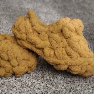 May include: A pair of fuzzy, mustard yellow knitted slippers. The slippers are made of a thick, chunky yarn and have a casual, comfortable look.