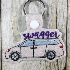 May include: A light pink glittery car-shaped keychain with the word "swagger" in purple script. The keychain has a silver key ring and a white snap closure. The car design includes black wheels and blue tinted windows.