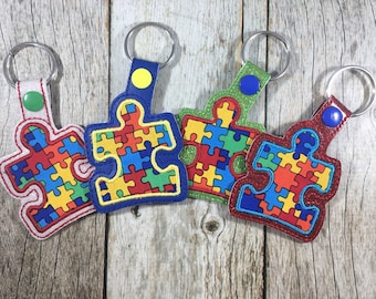 May include: Four colorful puzzle piece keychains. Each keychain features a puzzle piece design with a variety of colors, including red, blue, yellow, and green. The keychains have a metal ring for attaching keys.