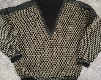 May include: A vintage sweater with a black turtleneck and a V-neck design. The sweater features a textured pattern in shades of black and gold, with black leather accents on the shoulders. The cuffs and hem are black.