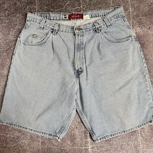 May include: Light blue denim shorts with a loose fit. The shorts have a classic five-pocket design, a button and zipper closure, and belt loops. The shorts are made of a light wash denim material and feature the word "LOOSE" on the label.