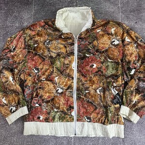 May include: A reversible jacket with a floral pattern in shades of brown, red, and green. The jacket has a white collar, cuffs, and hem, and a white zipper down the front. The jacket is a vintage style.