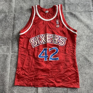 May include: Red basketball jersey with white and blue trim. The jersey has the word "SIXERS" in blue and white letters and the number "42" in blue letters on the front.