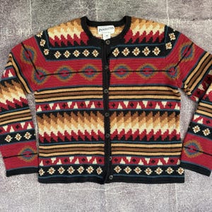 May include: A long-sleeve button-down cardigan featuring a multi-colored geometric pattern in red, black, tan, and blue. The knit garment has a round neckline, a black button placket, and a Pendleton brand label at the inner collar.