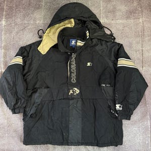 May include: A black Starter pullover jacket featuring a hood with a tan lining, long sleeves with tan and black stripes, and the text COLORADO printed vertically. The front displays a buffalo graphic, a Starter logo, and a high collar.