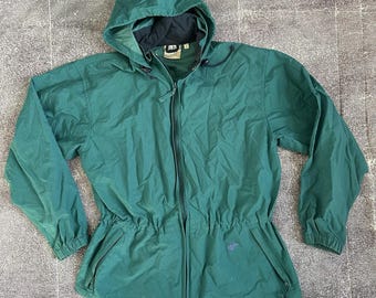 May include: A green hooded jacket with a full-length zipper, drawstring waist, and two front pockets. The jacket has a black lining in the hood and collar. The jacket is made of a lightweight material.