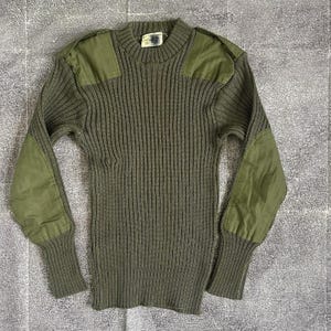 Peut inclure: Un pull en tricot vert avec des empiècements aux coudes. Le pull a une texture côtelée et un col rond.