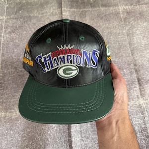 以下が含まれることがあります： 緑色のつばが付いた黒いレザー製の野球帽。Super Bowl Championsの刺繍文字とグリーンベイ・パッカーズのロゴが施されています。サイドパネルには、XXXI Championsと書かれた追加の刺繍パッチが付いています。