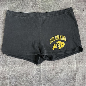May include: Black athletic shorts with an elastic waistband. The shorts feature the word "COLORADO" in gold arched lettering, with a gold graphic below. The shorts are made of a soft material.