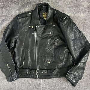 以下が含まれることがあります： 黒い革のバイカージャケット。斜めのジッパー、複数のポケット、ウエストベルトが付いています。肩と袖にはキルティングデザインがあります。襟にはスナップボタンがあり、裏地には「PROTECT LEATHER APPAREL」と書かれたタグが付いています。