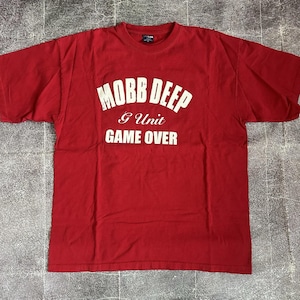 May include: Red t-shirt with the text "MOBB DEEP" above "G Unit GAME OVER" in white block letters. The shirt is a crew neck style and appears to be made of cotton. The shirt is laid flat on a textured surface.