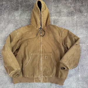 Op de afbeelding: Bruine jas met capuchon, een ritssluiting over de hele lengte, een kangoeroezak en geribde manchetten en zoom. De jas heeft een capuchon met trekkoord en een klein logo op de borst. De jas is gemaakt van een duurzame stof in workwear-stijl.