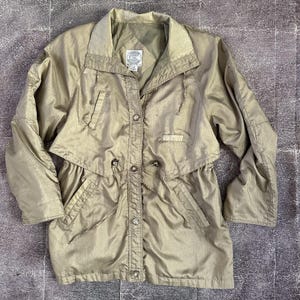 May include: A vintage gold-toned jacket with a unique design. It features a collared neckline, button-up front, and a cinched waist with a drawstring. The jacket has pockets and a layered design, giving it a retro aesthetic.