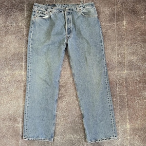 Könnte beinhalten: Hellblaue Jeans aus Denim mit Knopfleiste und klassischem Fünf-Taschen-Design. Die Jeans haben eine gerade Beinpassform und weisen Gebrauchsspuren auf, was ihnen einen Vintage-Look verleiht. Die Jeans sind mittelblau gewaschen und scheinen getragen worden zu sein.