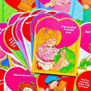 May include: A collection of heart-shaped Valentine's Day cards featuring illustrations of Cabbage Patch Kids dolls. The cards display various colorful designs with phrases such as I'm so glad I found you, You're one of a kind, and You're terrific from top to toes.