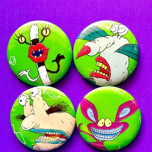 Puede incluir: Cuatro botones redondos verdes con diseños de personajes de dibujos animados. Cada botón presenta un personaje diferente con contornos audaces y colores brillantes. Los personajes tienen rasgos exagerados, incluyendo ojos, bocas y dientes grandes. Los botones están sobre un fondo púrpura.