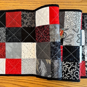 May include: A black and white table runner with red squares. The runner is made of fabric with different patterns, including floral, geometric, and paisley.