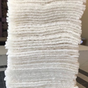 May include: A stack of white batting squares, a type of fabric used for quilting and crafts.