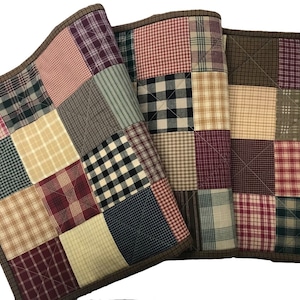May include: Three brown-trimmed patchwork table runners with a variety of plaid patterns in red, green, black, and white.