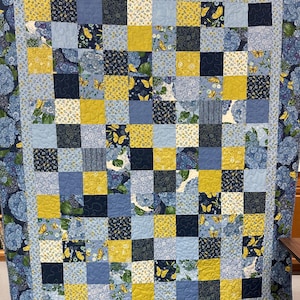 May include: A quilt with a patchwork design featuring squares of blue, yellow, and white fabric. The fabric has a floral pattern with butterflies.
