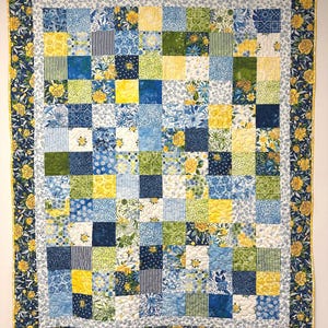May include: A patchwork quilt with a floral design. The quilt features squares in shades of blue, yellow, and green. The border is a dark blue with yellow flowers. The quilt is approximately 70 inches by 80 inches.