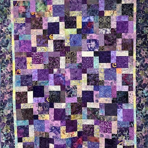 May include: A handmade quilt featuring a patchwork design in various shades of purple, lavender, and blue. The quilt has a floral border and a yellow inner border. The squares have different patterns and textures, creating a visually rich and cozy textile.
