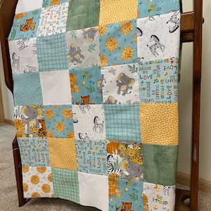 May include: A patchwork quilt featuring a repeating pattern of safari animals including elephants, lions, tigers, and zebras. The fabric squares are in shades of teal, yellow, white, and green, with text prints that read Be Proud, Love, and Unique.
